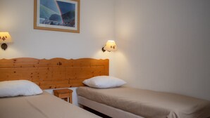 Een kamer met twee éénpersoonsbedden, een houten hoofdbord, een klein nachtkastje en een lijst met een afbeelding aan de muur.