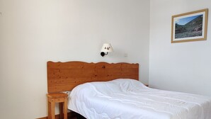A bedroom with a wooden bed, a nightstand, a wall-mounted lamp, and a framed picture on the wall. - 3-room apartment for 6 people, mountain view, pets allowed (Le Dévoluy)