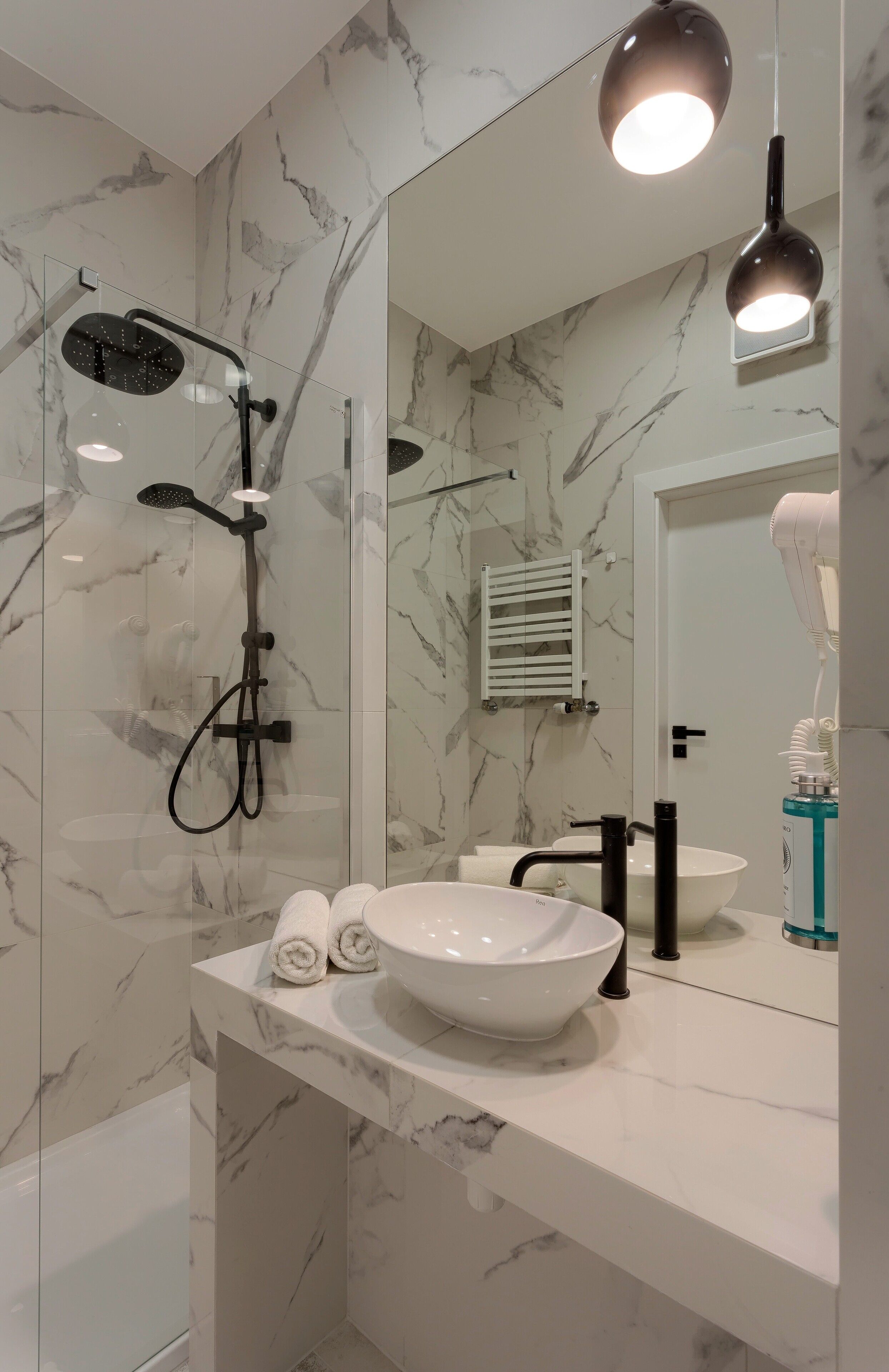 Un baño moderno con ducha de vidrio, lavamanos de mármol blanco y un espejo grande.