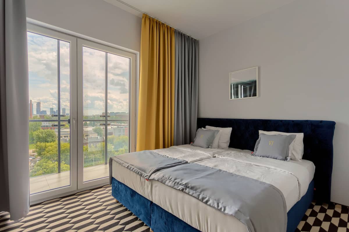 A hotel room with a large bed, a view through a sliding door, and a checkered floor.