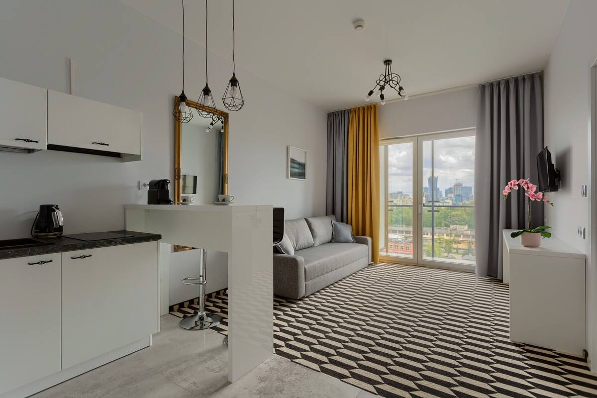 A modern apartment with a kitchen, a sofa, and a large window with a city view.