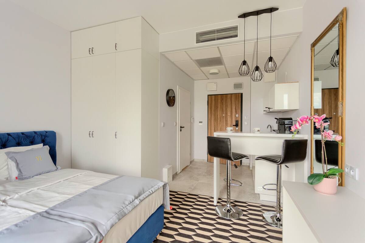 A modern bedroom with a bed, wardrobe, and a kitchenette area.