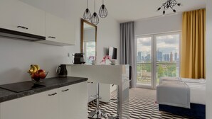 Een moderne hotelkamer met een kitchenette, een eettafel, een bed en een groot raam met uitzicht op de stad.