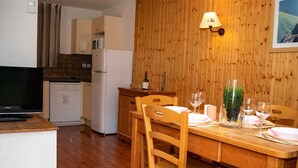 A wooden dining table set with chairs, a television, and kitchen appliances in the background. - Semi-Detached Chalet 3 Rooms 6 Pers, Pets Allowed (Le Dévoluy)