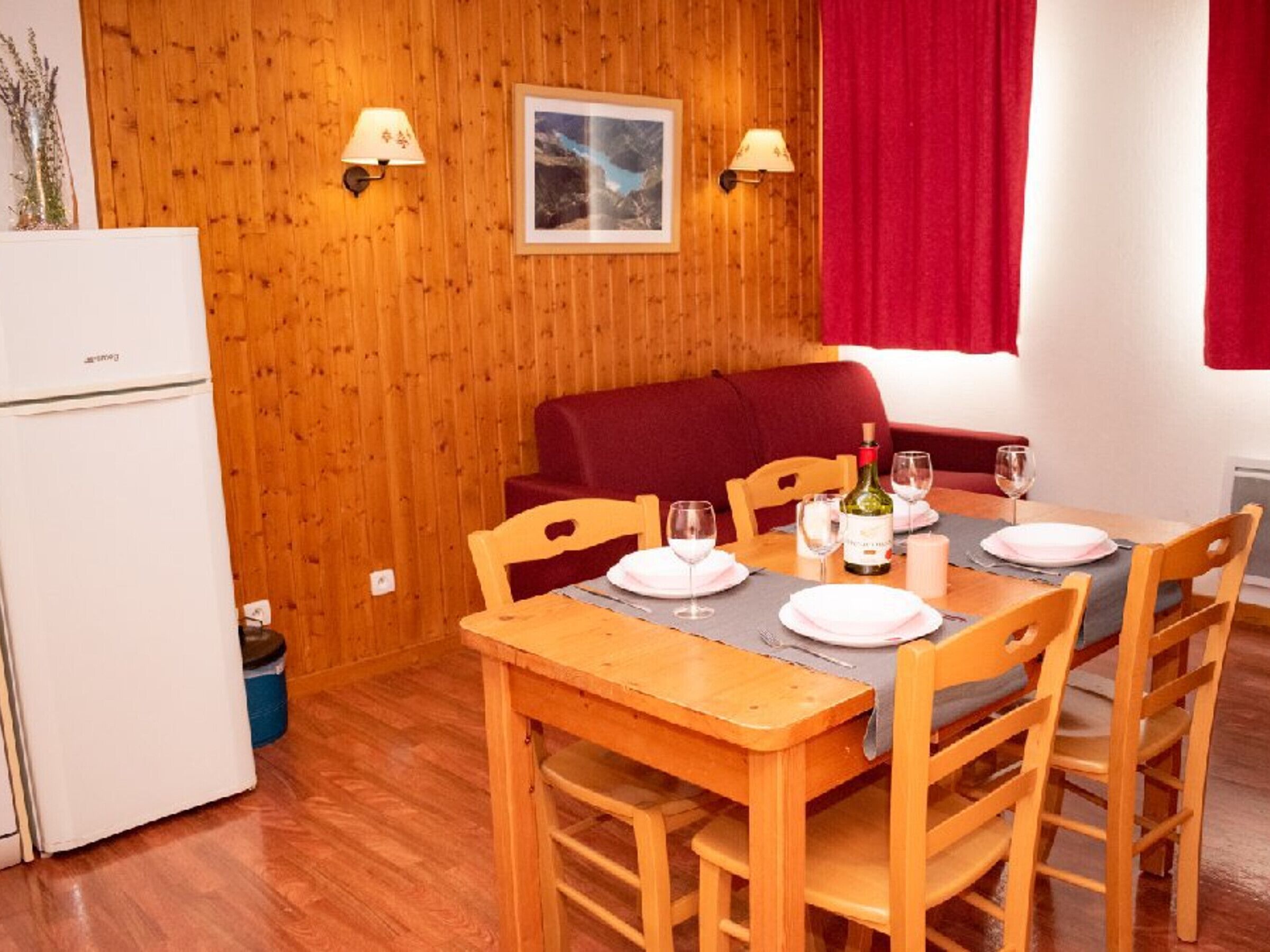 Un coin repas avec une table en bois dressée pour quatre personnes, un canapé rouge et un réfrigérateur blanc.