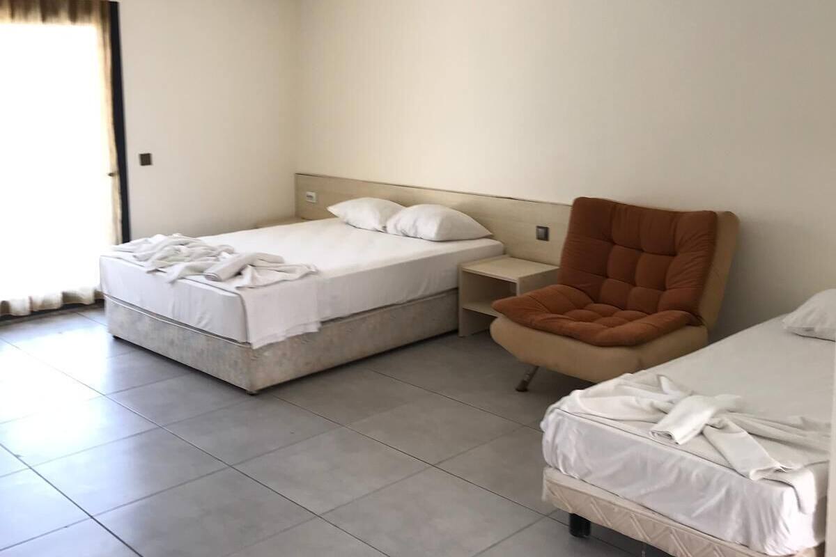 A hotel room with two beds, a brown armchair, and a small bedside table.