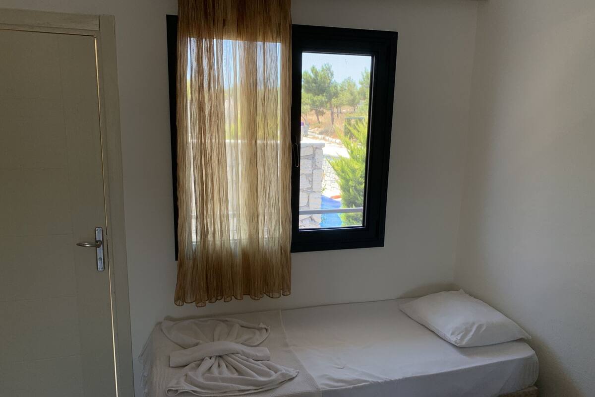 A small, single-bed room with a window overlooking a garden.