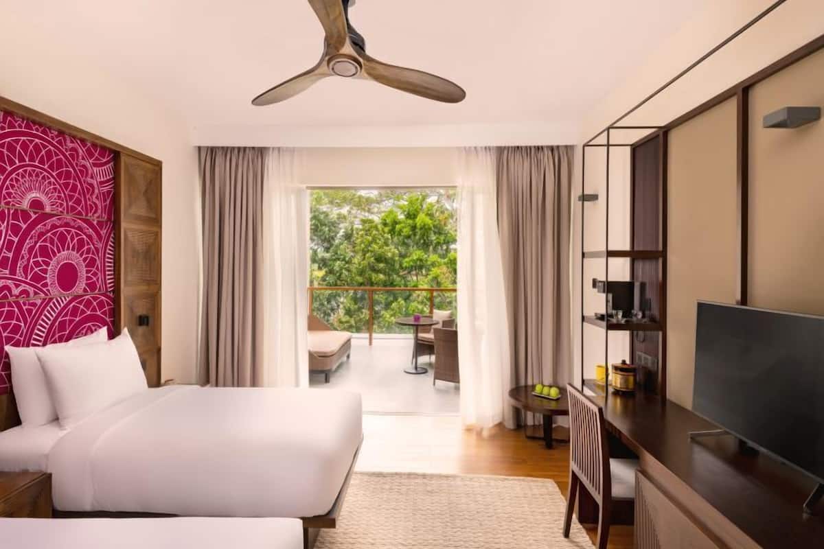 A hotel room with a bed, a desk, a TV, and a balcony with a view of greenery.