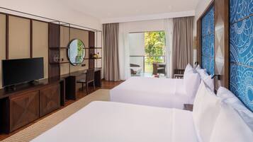 A hotel room with two beds, a TV, a desk, and a large window with a view of greenery.