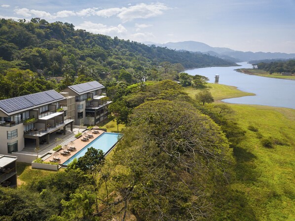 A modern hotel with a swimming pool, surrounded by lush greenery and a view of a lake.