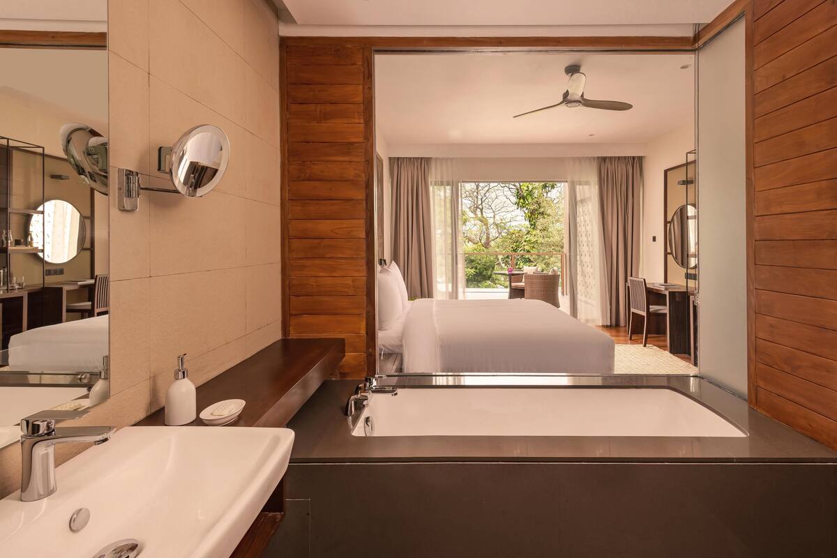 A modern hotel room with a large mirror, a bathtub, a sink, and a bed.