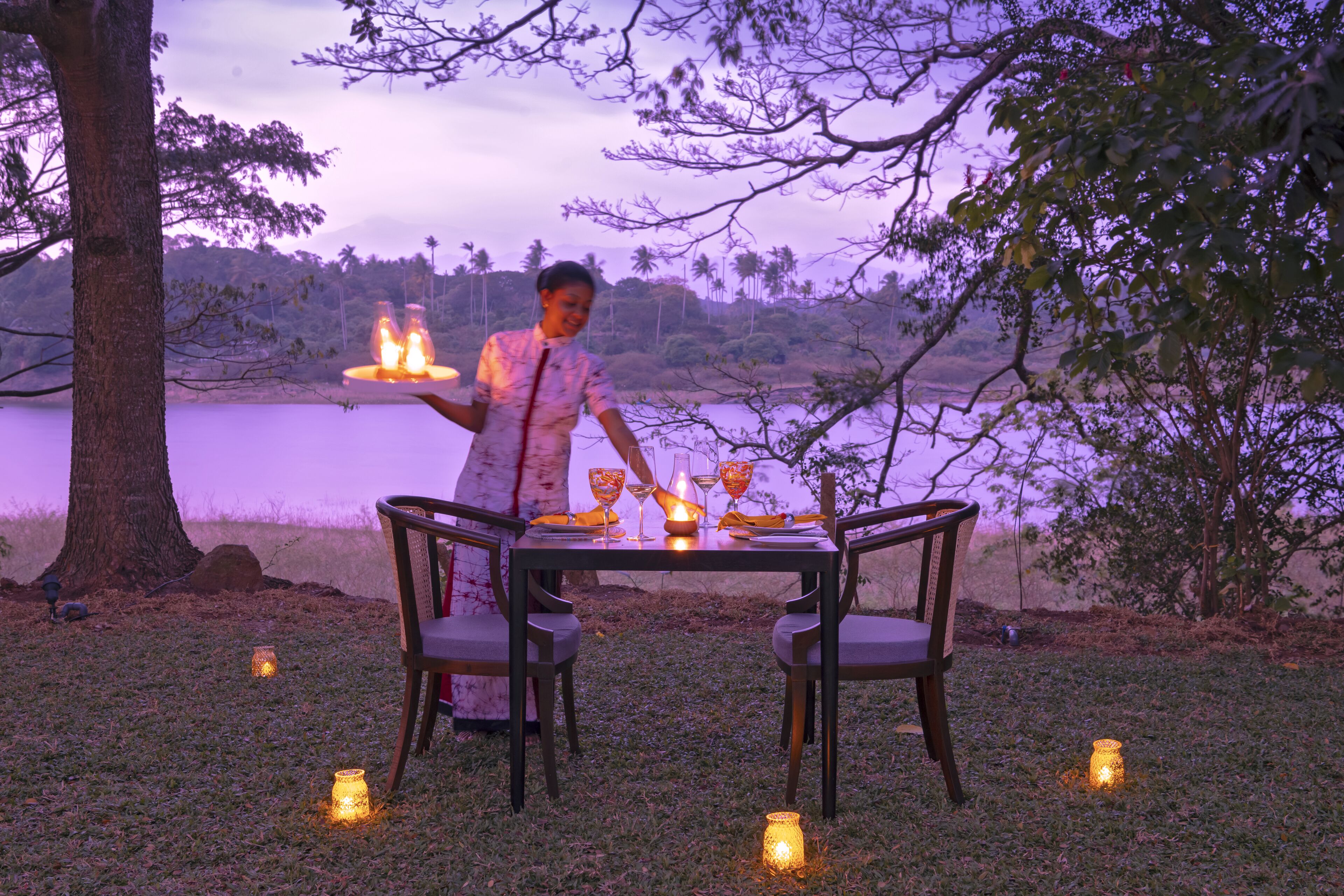 An outdoor dining setup with a table and chairs, surrounded by trees and a body of water.