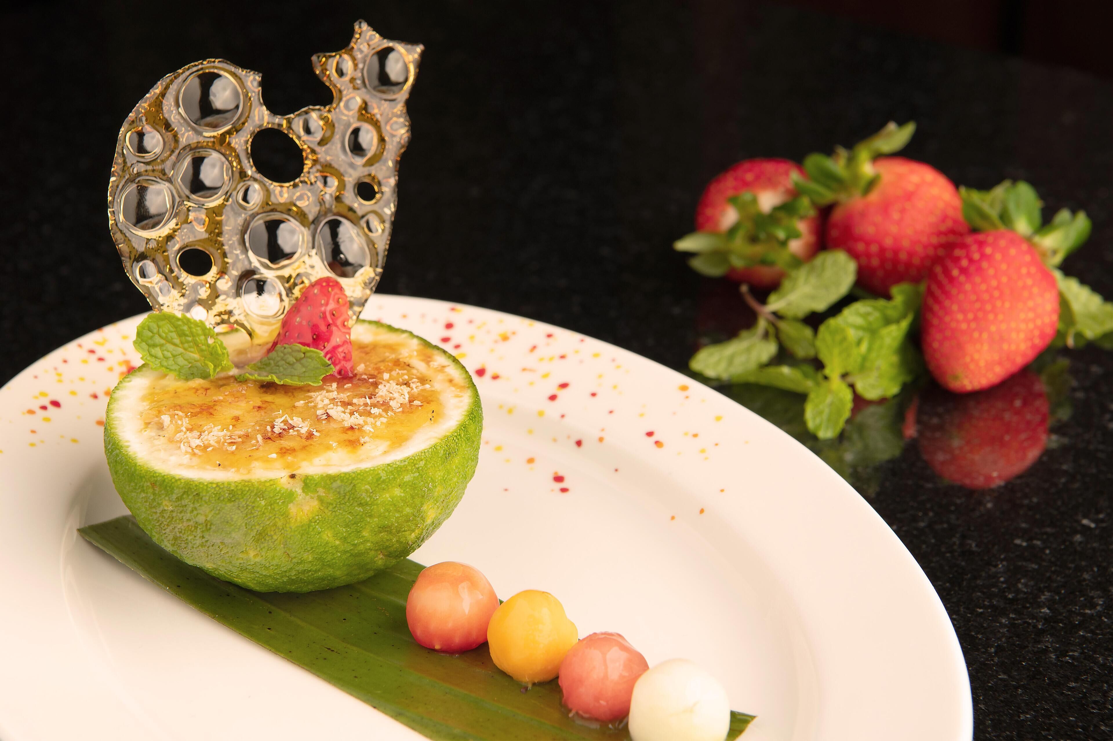 A fruit-based dessert on a plate with a decorative metal piece and strawberries in the background.