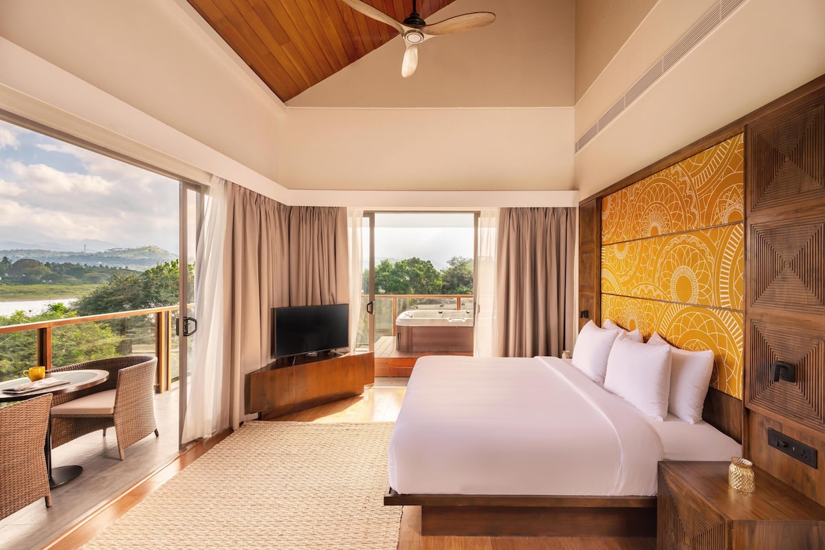 A spacious bedroom with a large bed, a television, and a balcony with a hot tub.