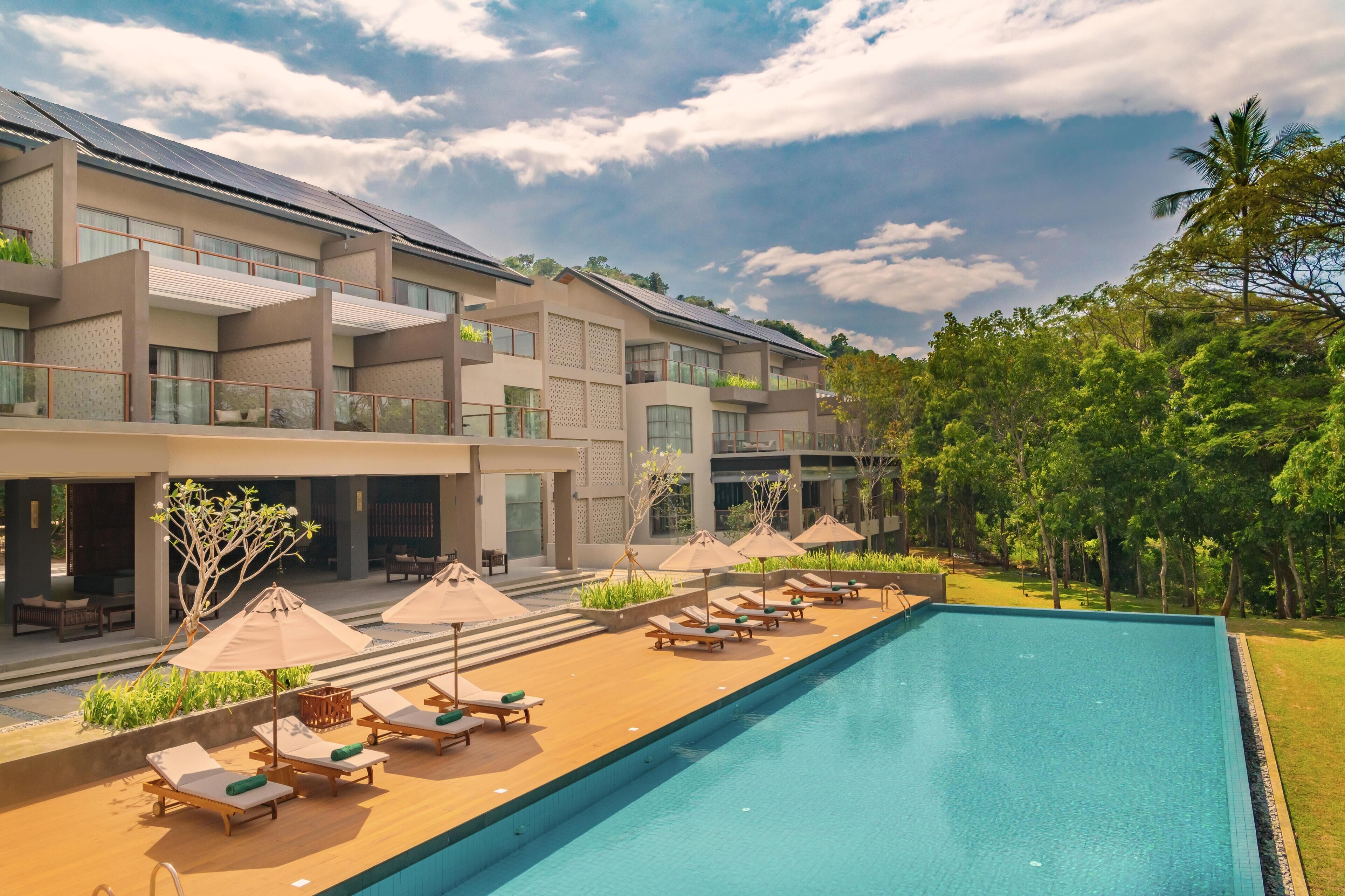 A hotel with a swimming pool, sun loungers, and umbrellas.