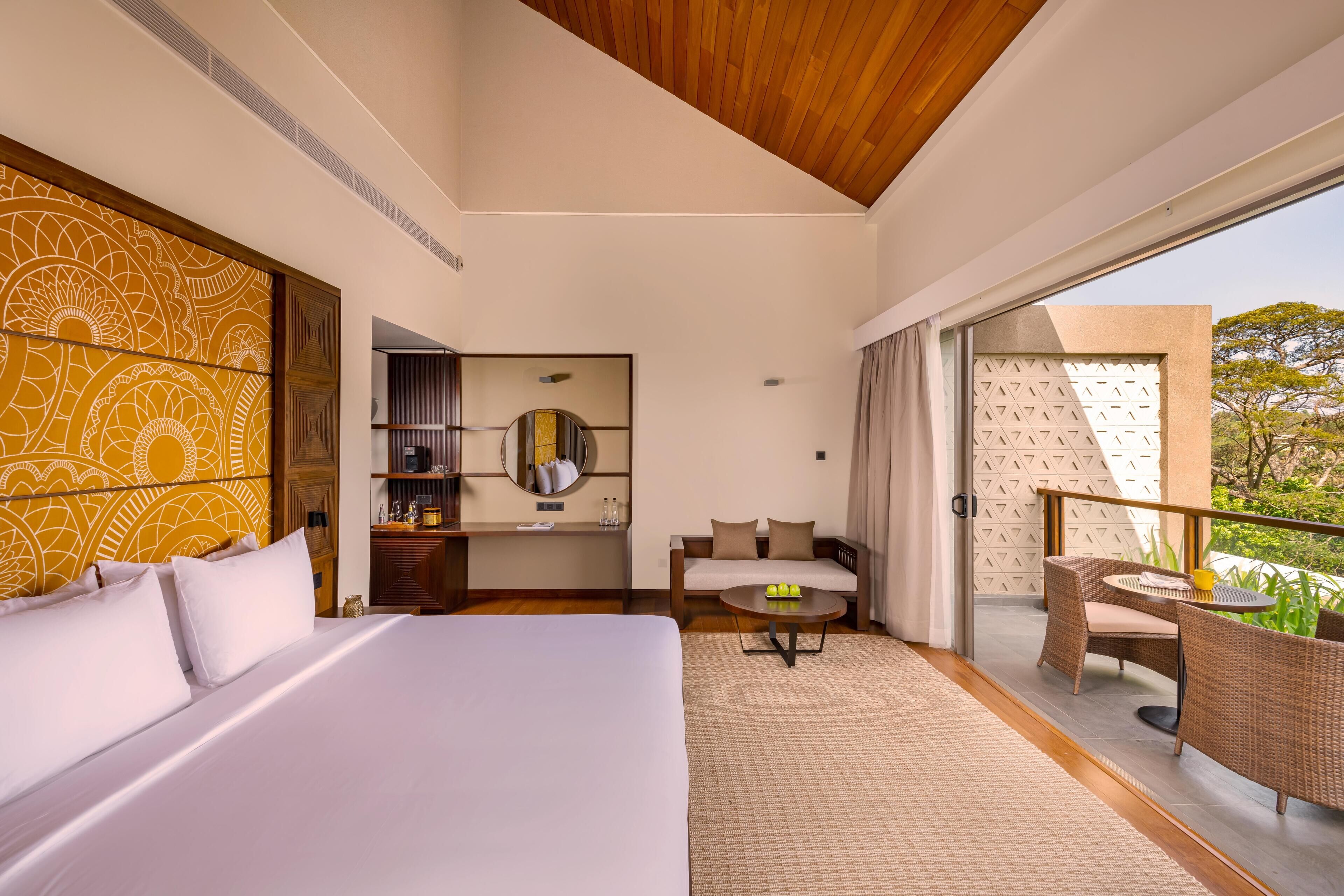 Een hotelkamer met een groot bed, een bank, een eettafel en een balkon met rieten meubels.