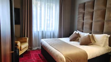 A hotel room with a large bed, a red patterned carpet, a sofa, and a window with sheer curtains.