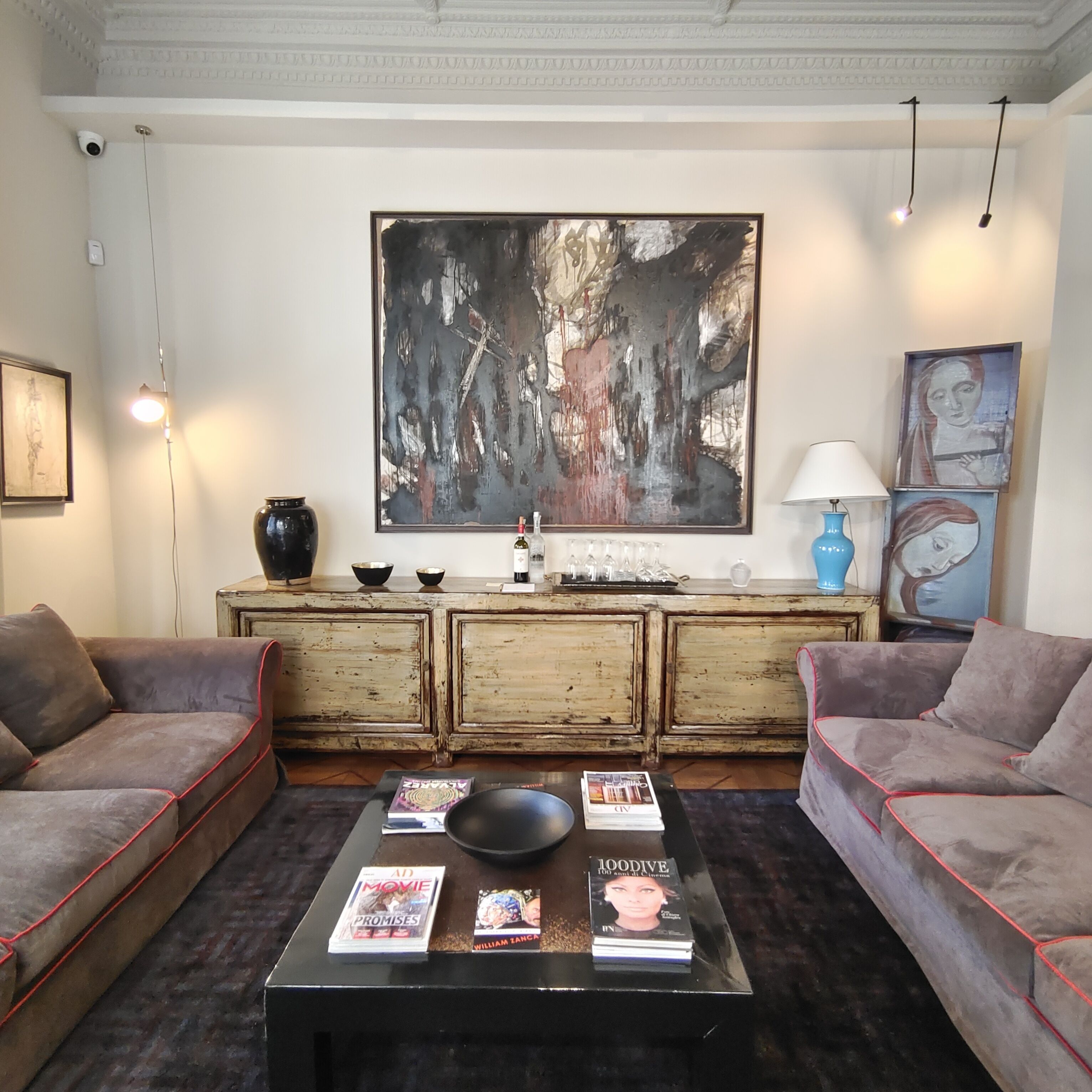 A living room with two sofas, a coffee table with magazines, a large abstract painting, and a rustic wooden cabinet.