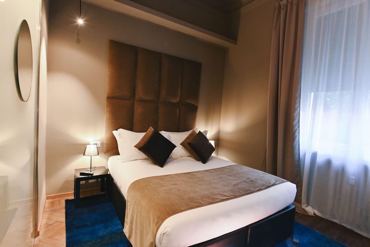 A hotel room with a large bed, a nightstand with a lamp, and a window with curtains.