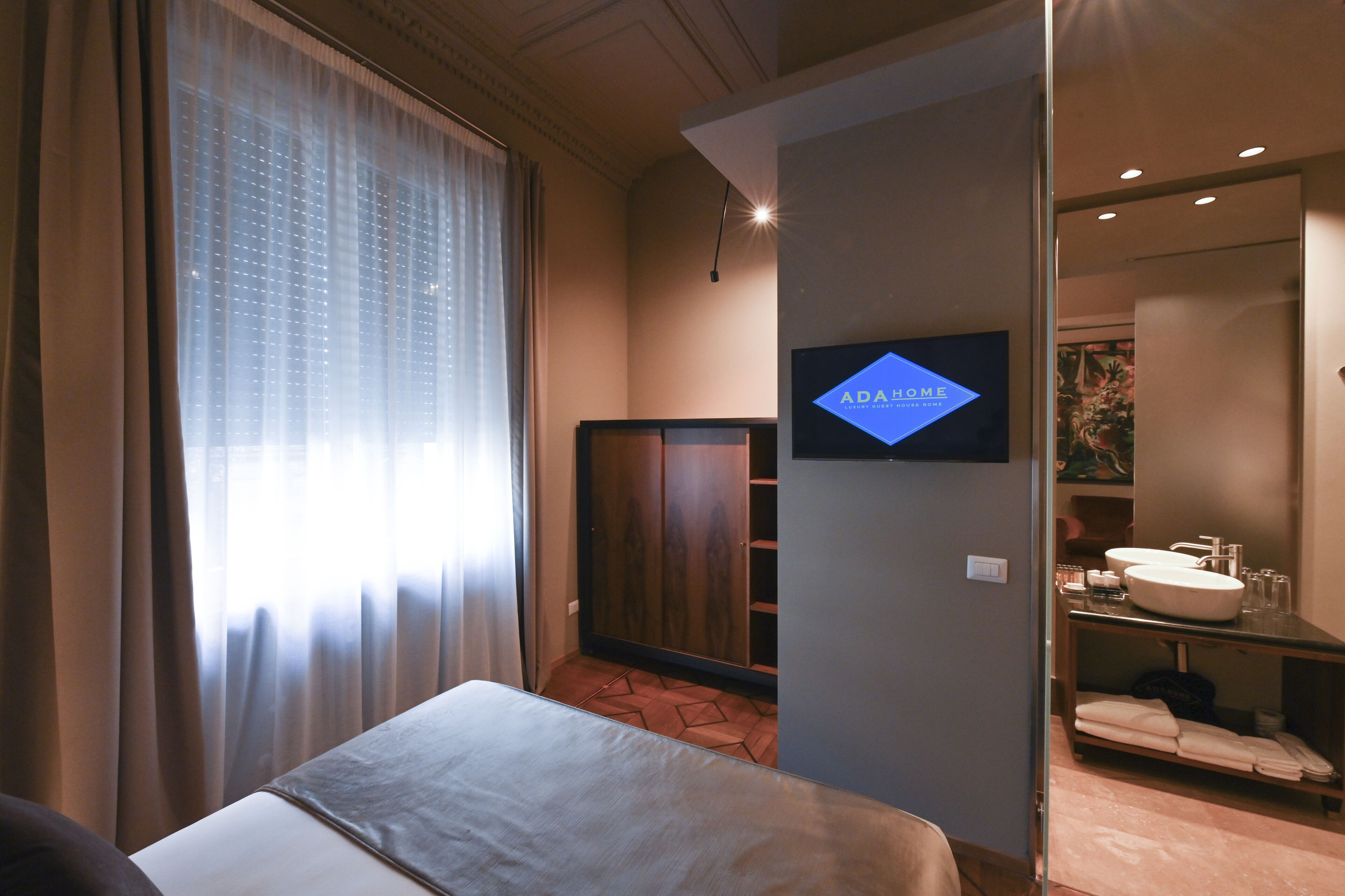 A hotel room with a bed, a television, a wardrobe, and a bathroom with a sink and mirror.