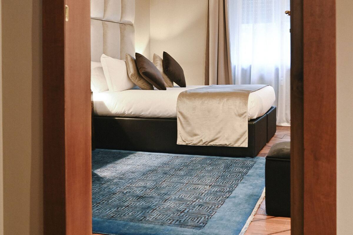 A bedroom with a bed, a blue patterned rug, and a wooden door frame.