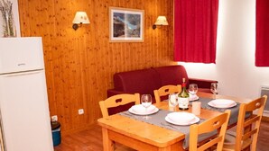 A dining area with a wooden table set for four, a red sofa, and a white refrigerator. - 3-room apartment, balcony, pets allowed (Le Dévoluy)