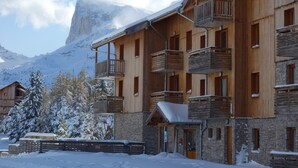 Un edificio de madera de varios pisos con balcones, fachada de piedra y una montaña nevada al fondo.