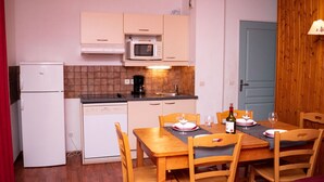 Una cocina compacta con microondas, cafetera y refrigerador pequeño. Hay una mesa de comedor con sillas y una botella de vino encima.