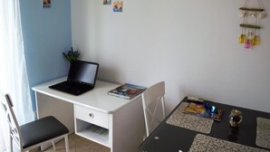 A small, neatly arranged room with a white desk, a laptop, a chair, a table with a magazine, and a wall decoration. - Leela Apartment (Dubrovnik)
