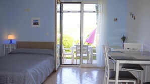 A bedroom with a bed, a desk, and a chair, and a sliding glass door leading to an outdoor area with a table and chairs. - Leela Apartment (Dubrovnik)