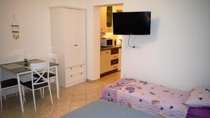 A small, well-lit room with a bed, a desk with a chair, a wardrobe, and a television mounted on the wall. - Leela Apartment (Dubrovnik)