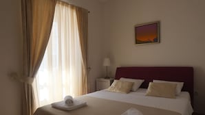 Een net opgemaakt bed met witte lakens en een rode hoofdbord, een bedlamp en een schilderij van een zonsondergang aan de muur.