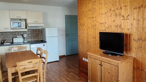 Une cuisine compacte avec des meubles en bois, un four à micro-ondes, un grille-pain et un réfrigérateur. On y trouve une table à manger avec des chaises et un téléviseur posé sur un meuble en bois.