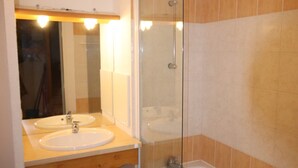Une salle de bain avec deux lavabos, une douche en verre et des murs recouverts de carreaux beiges.