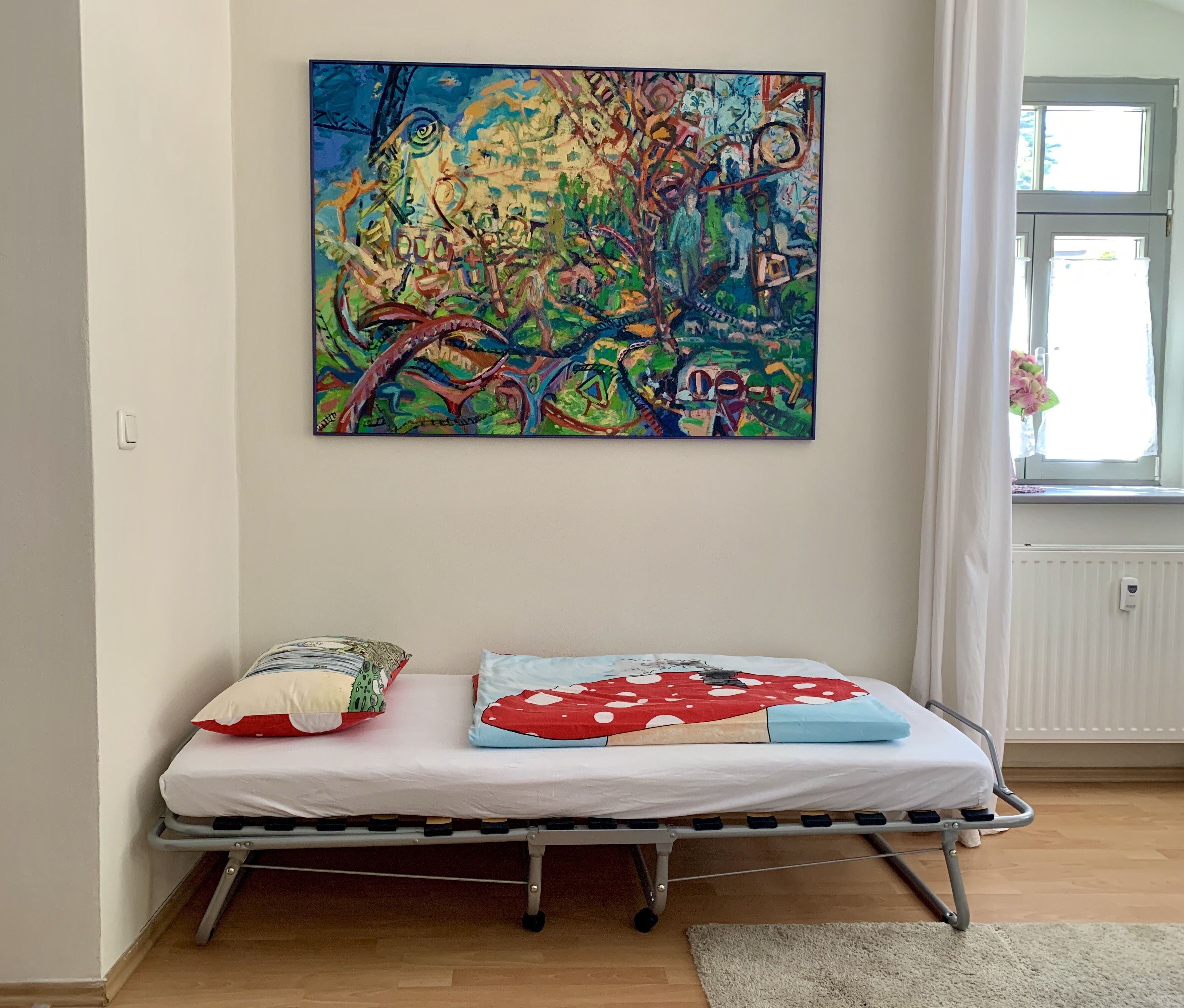 Ein Zimmer mit einem Bett, einem farbenfrohen abstrakten Gemälde an der Wand und einem Fenster mit Vorhängen.