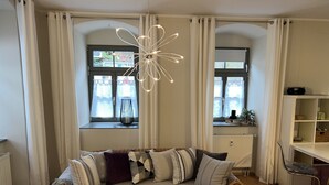 A living room with a sofa, a coffee table, a bookshelf, and a window with curtains. - Stadthaus Rosengasse (Meissen)