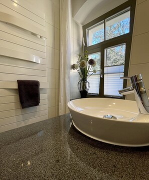 A bathroom with a round sink, a towel rack, and a window with blinds.