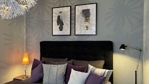A neatly arranged bedroom with a bed, pillows, a nightstand, a lamp, and two framed artworks on the wall. - Stadthaus Rosengasse (Meissen)