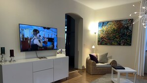 A modern living room with a flat-screen TV, a wicker sofa, a white coffee table, and a painting on the wall. - Stadthaus Rosengasse (Meissen)