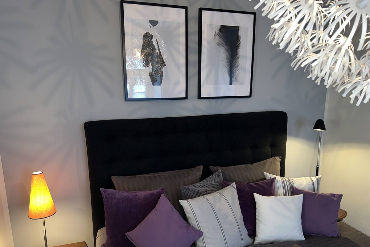 A bedroom with a bed, pillows, a lamp, and two framed artworks on the wall.