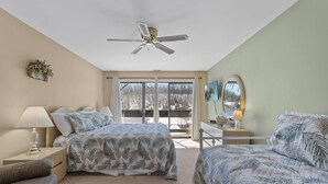 Une chambre avec deux lits, un ventilateur de plafond, une grande fenêtre avec vue, un bureau avec un miroir et une lampe.