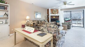 Un salon comprenant un canapé, une table avec un panneau, une lampe, une cheminée et une vue sur l’extérieur.