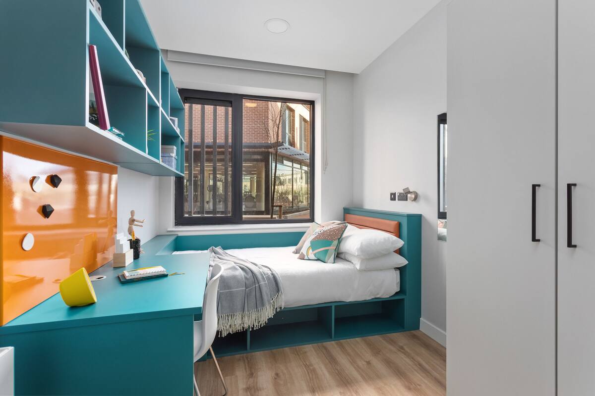 Une chambre moderne aux couleurs turquoise, dotée d’une grande fenêtre et d’un lit agrémenté de nombreux coussins.