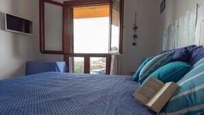 A bedroom with a bed, a book, and a window with a view of buildings. - Bella Vista (Trinità d'Agultu e Vignola)
