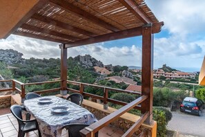 A covered outdoor seating area with a table and chairs, overlooking a scenic landscape with rocky hills and buildings. - Bella Vista (Trinità d'Agultu e Vignola)