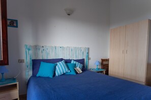 A bedroom with a bed, a wooden wardrobe, a nightstand, and a wall-mounted light fixture. - Bella Vista (Trinità d'Agultu e Vignola)