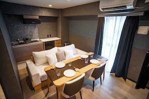 A compact hotel room with a kitchenette, a sofa bed, a dining table with chairs, and a large window with curtains. - Kabin Shiro - Regale Collection (Osaka)
