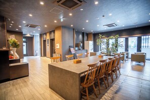 A modern hotel lobby with a central island table, wooden chairs, a reception desk, and a large window offering a view of the city. - Kabin Shiro - Regale Collection (Osaka)