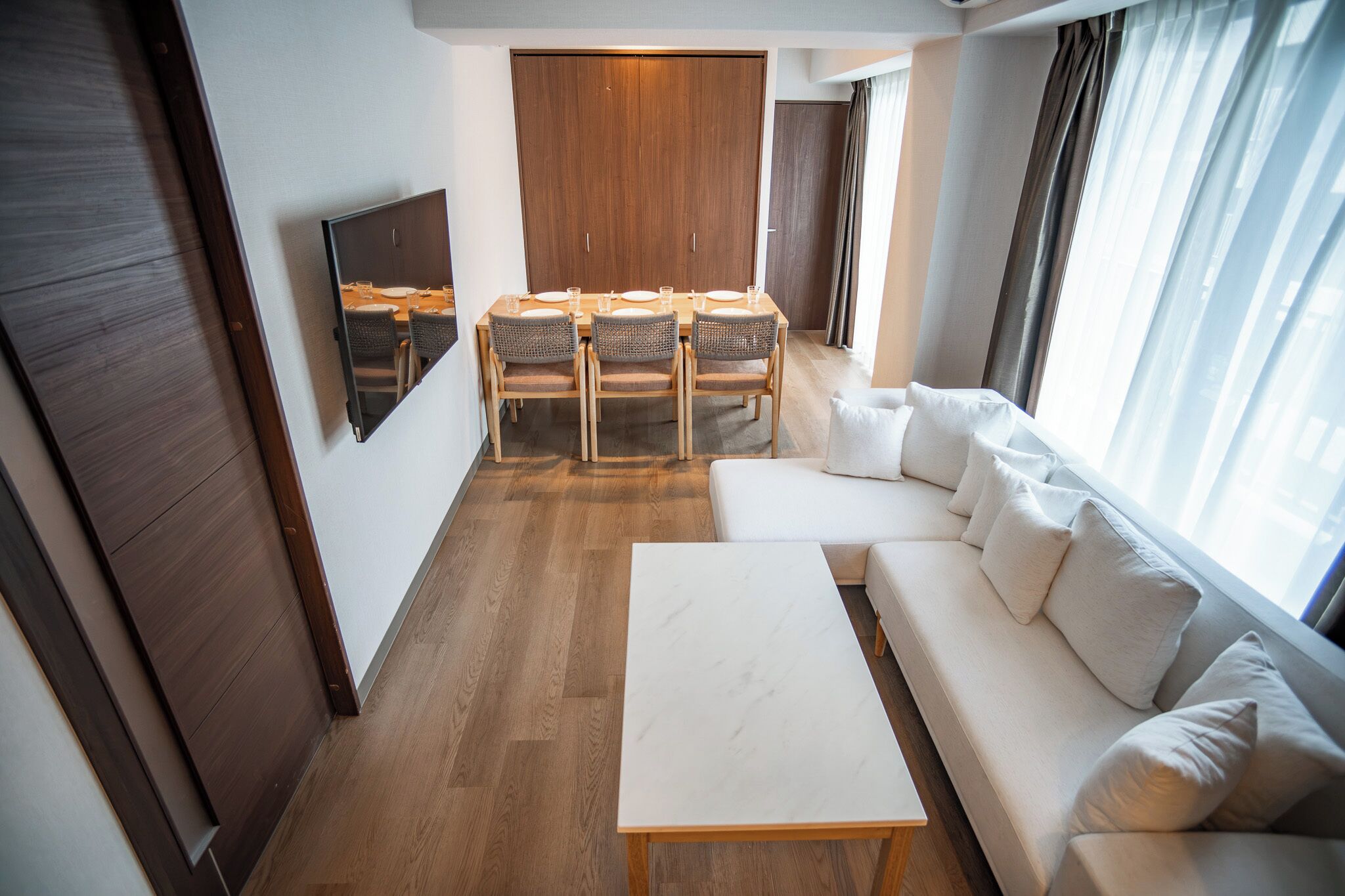 A modern hotel room with a dining area, a sofa, and a TV.