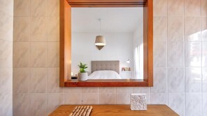 Une chambre à coucher avec un grand miroir, une table de chevet avec une lampe, une plante en pot et un lit avec une tête de lit blanche.